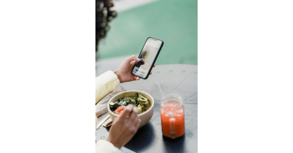 Crop Blogger with smartphone and tasty vegan salad in cafeteria. Taking salad photo for social media.