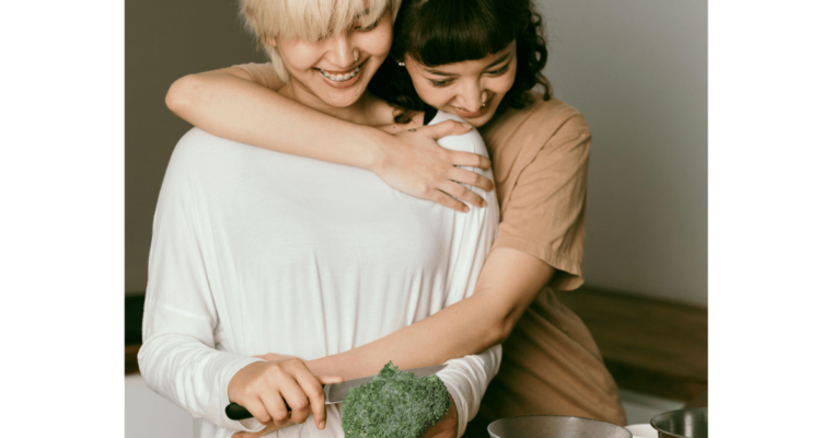 Woman cutting broccoli with daughter hugging her