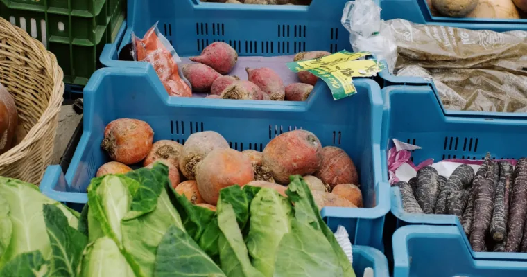 plastic boxes with various fresh vegetables for sale on market stall.