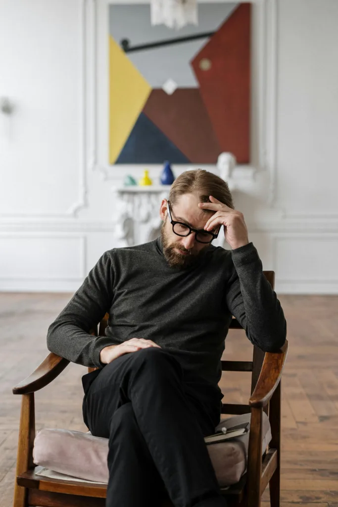 A man sitting on a brown wooden chair thinking a sign of men's mental health.